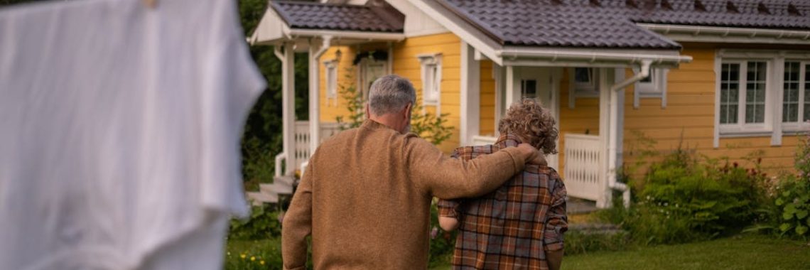 Grandfather and grandson walking together in a lush backyard with a charming house in the background.